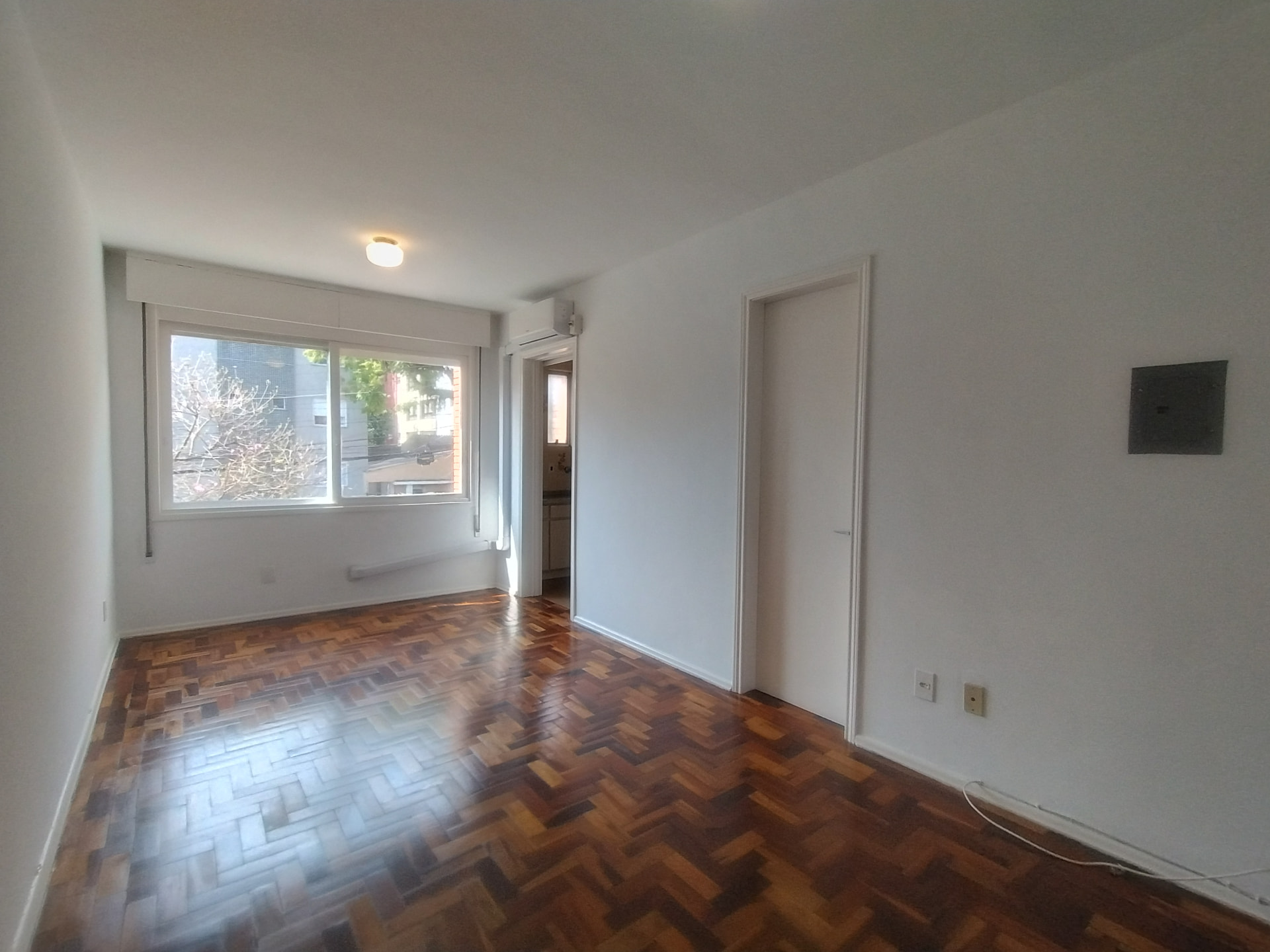 Sala de estar com piso em parquet espinha de peixe, janela ampla e ar-condicionado